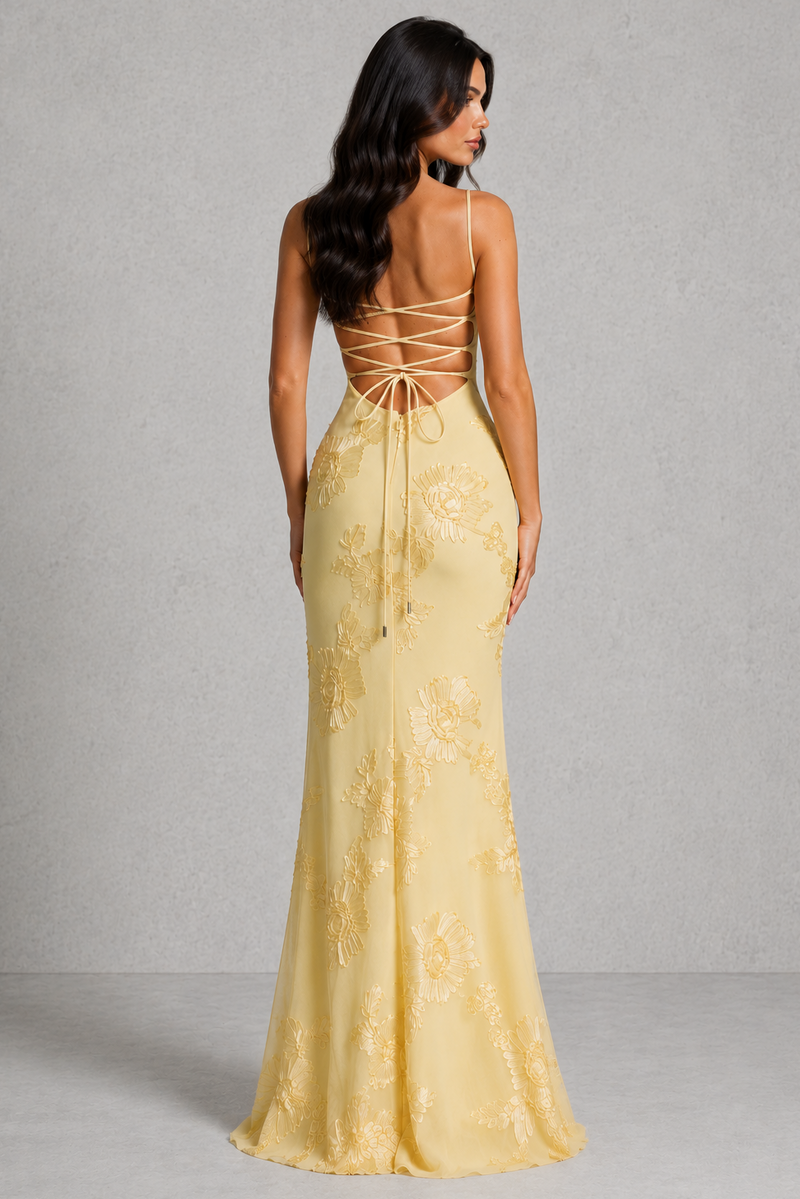 Woman wearing a yellow evening gown with lace-up back against a gray background