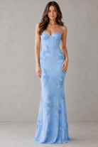 Woman wearing a light blue floral dress against a gray background
