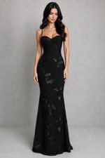 Woman wearing a black evening gown with floral lace details against a gray background