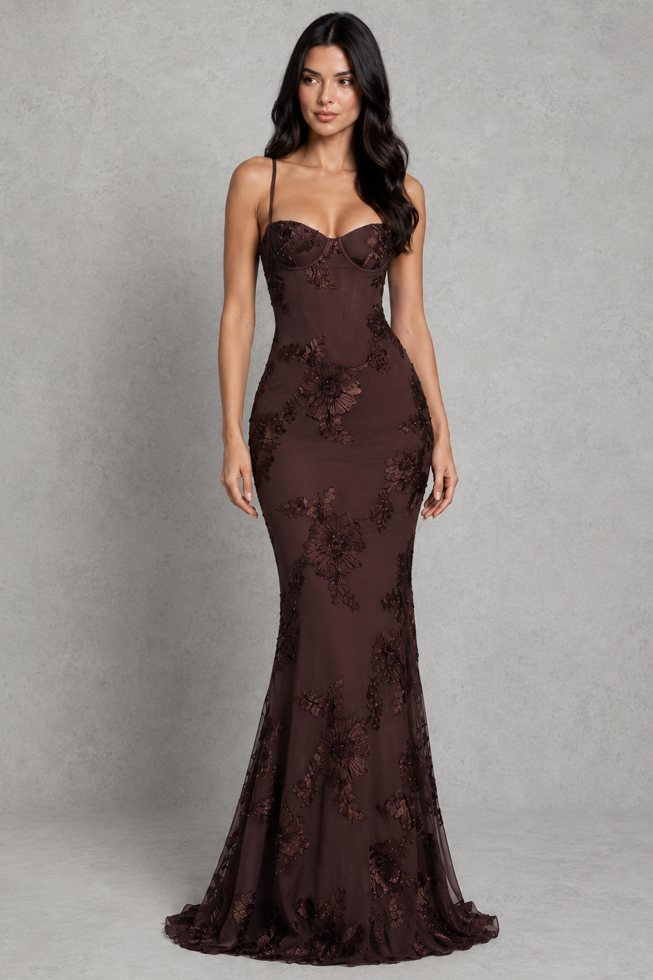 Woman wearing a dark brown evening gown with floral lace details on a gray background