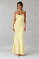 Woman wearing a light yellow evening gown against a gray background