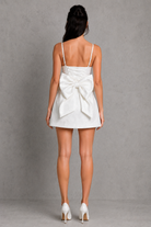Woman wearing a white dress with a large bow on a gray background