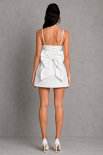 Woman wearing a white dress with a large bow on a gray background