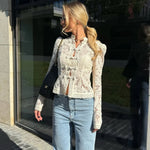Woman wearing a lace top and jeans standing in front of a reflective building facade.