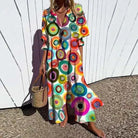 Woman wearing a colorful circular patterned dress against a white wooden fence.