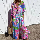Woman wearing a colorful floral dress against a white wall.