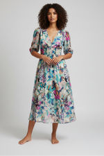 Woman wearing a colorful floral dress standing outdoors on stone steps.