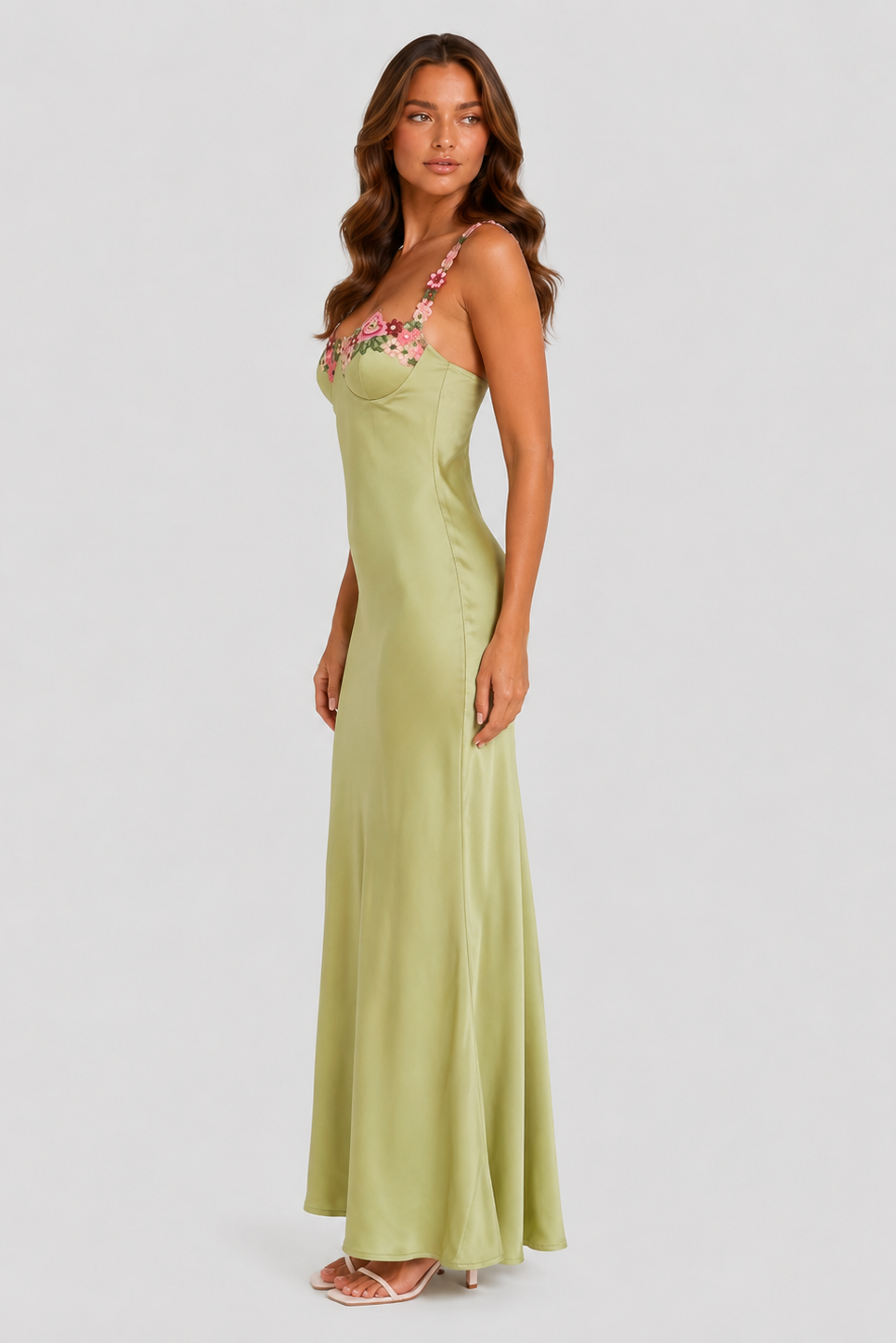 Woman wearing a long green dress with floral straps on a white background