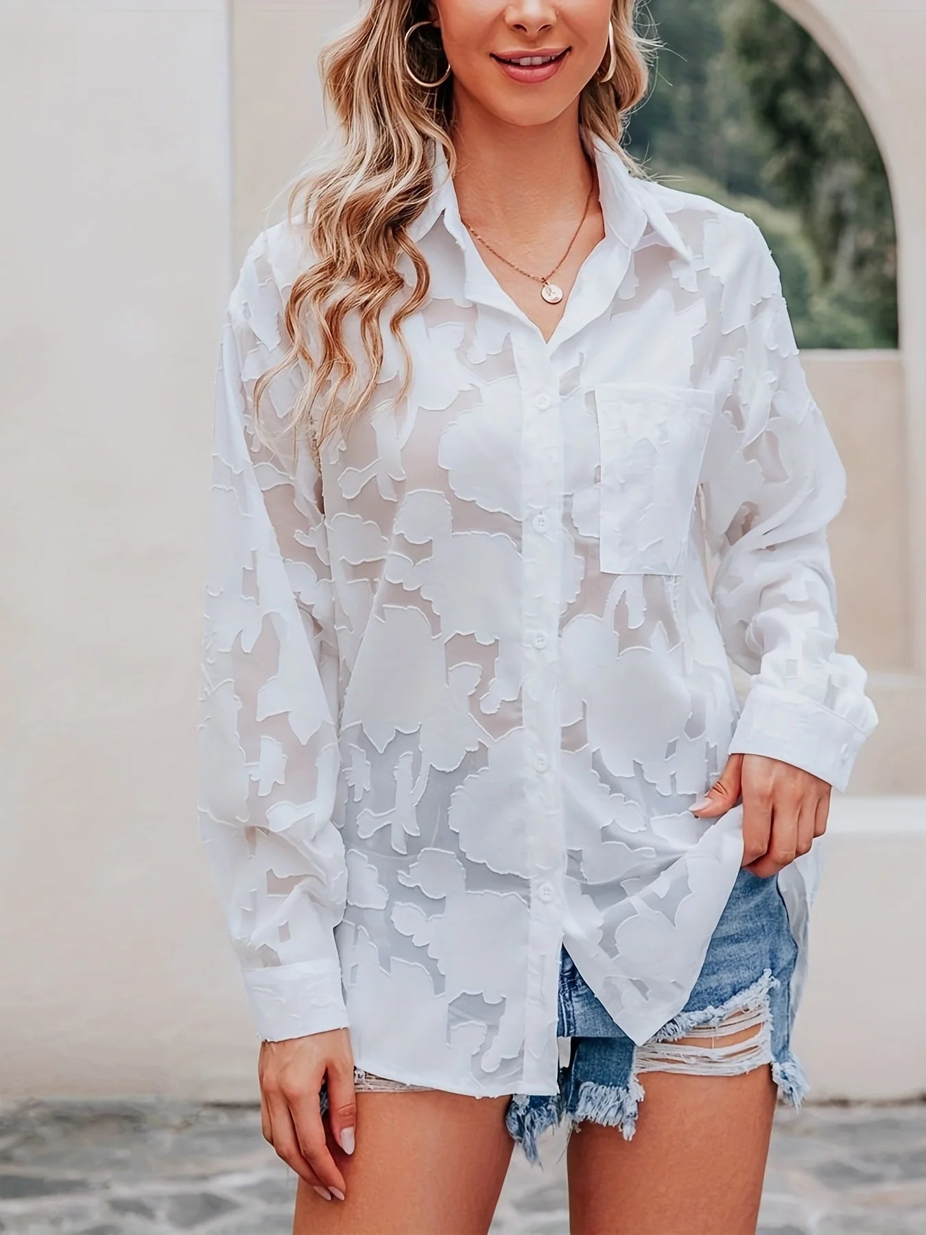 Woman wearing a white lace cover-up over denim shorts outdoors.