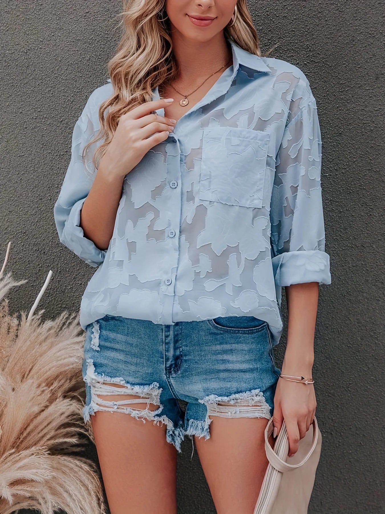 Woman wearing a light blue camouflage shirt and denim shorts against a gray background
