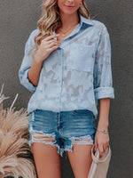 Woman wearing a light blue camouflage shirt and denim shorts against a gray background