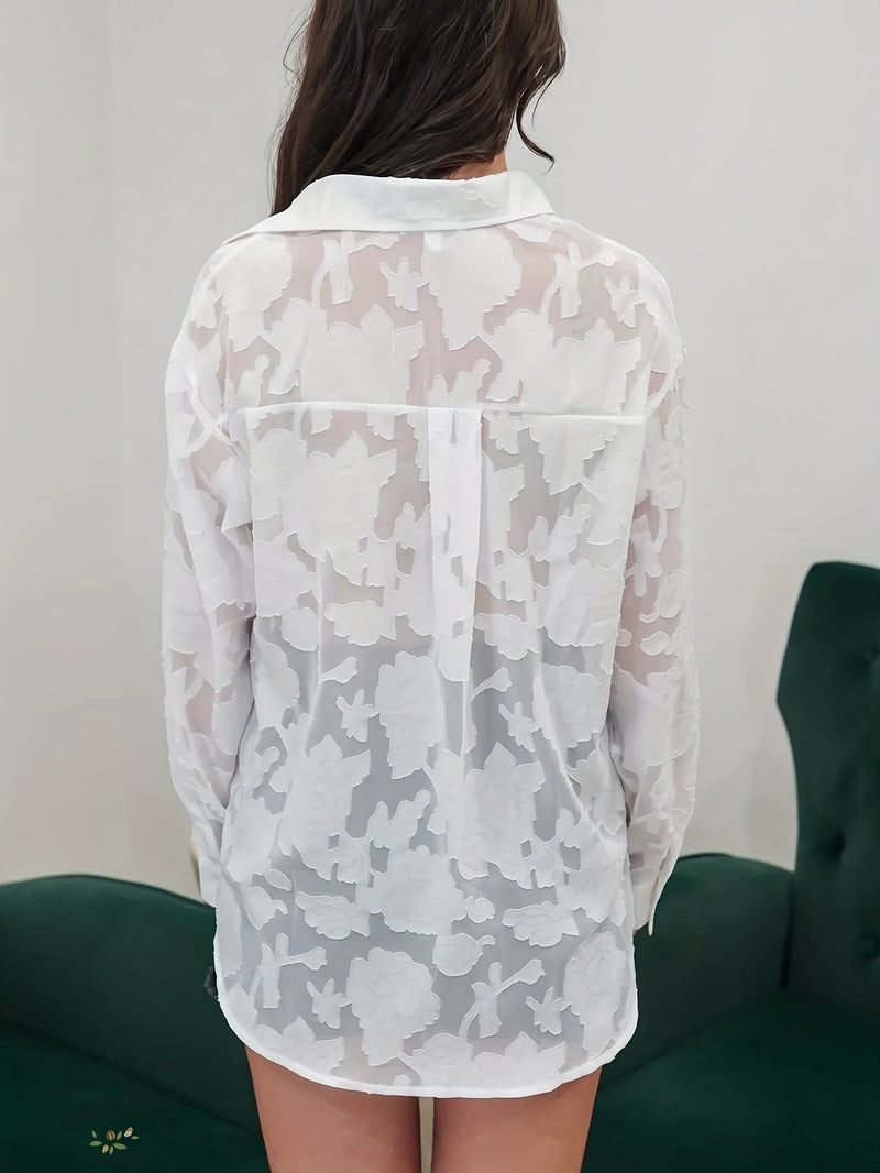 Person wearing a sheer floral blouse against a plain background