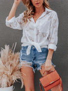 Woman wearing a white lace top and denim shorts, holding an orange handbag against a gray background.