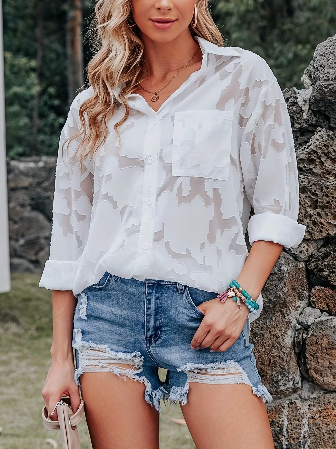 Woman wearing a white camouflage shirt and denim shorts standing outdoors.