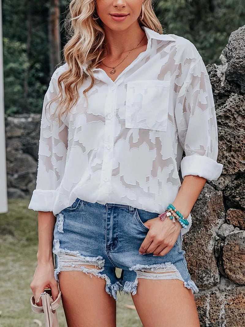 Woman wearing a white camouflage shirt and denim shorts standing outdoors.