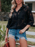 Woman wearing a black sheer blouse and denim shorts outdoors.