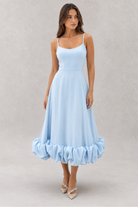 Woman wearing a light blue dress with ruffled hem on a plain background