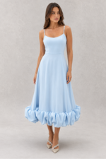 Woman wearing a light blue dress with ruffled hem on a plain background