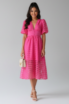 Woman wearing a pink dress standing indoors with a neutral background
