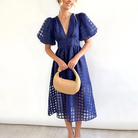 Woman wearing a blue dress holding a beige handbag against a white background