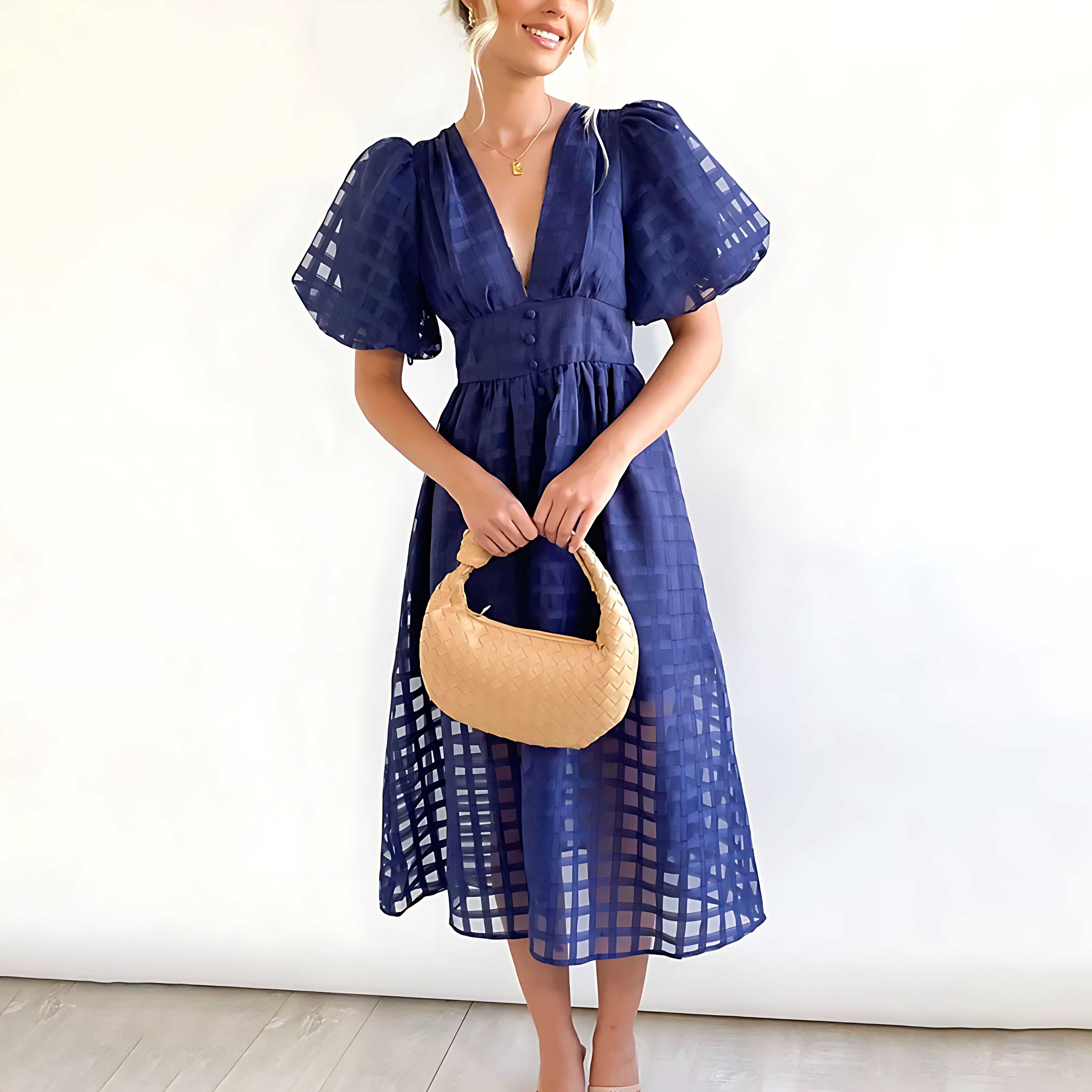 Woman wearing a blue dress holding a beige handbag against a white background