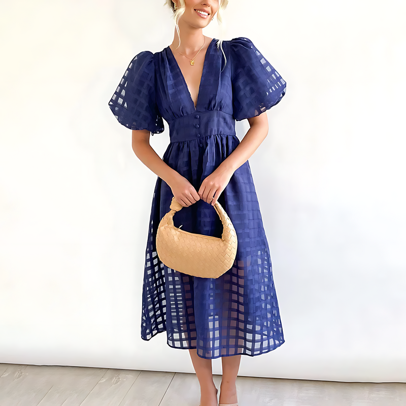Woman wearing a blue dress holding a beige handbag against a white background