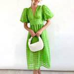 Woman wearing a green dress holding a white handbag against a white background