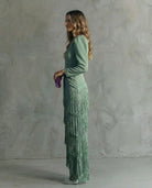 Woman in a green fringe dress holding a purple clutch against a gray background