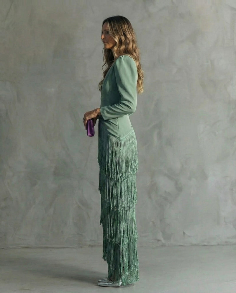 Woman in a green fringe dress holding a purple clutch against a gray background