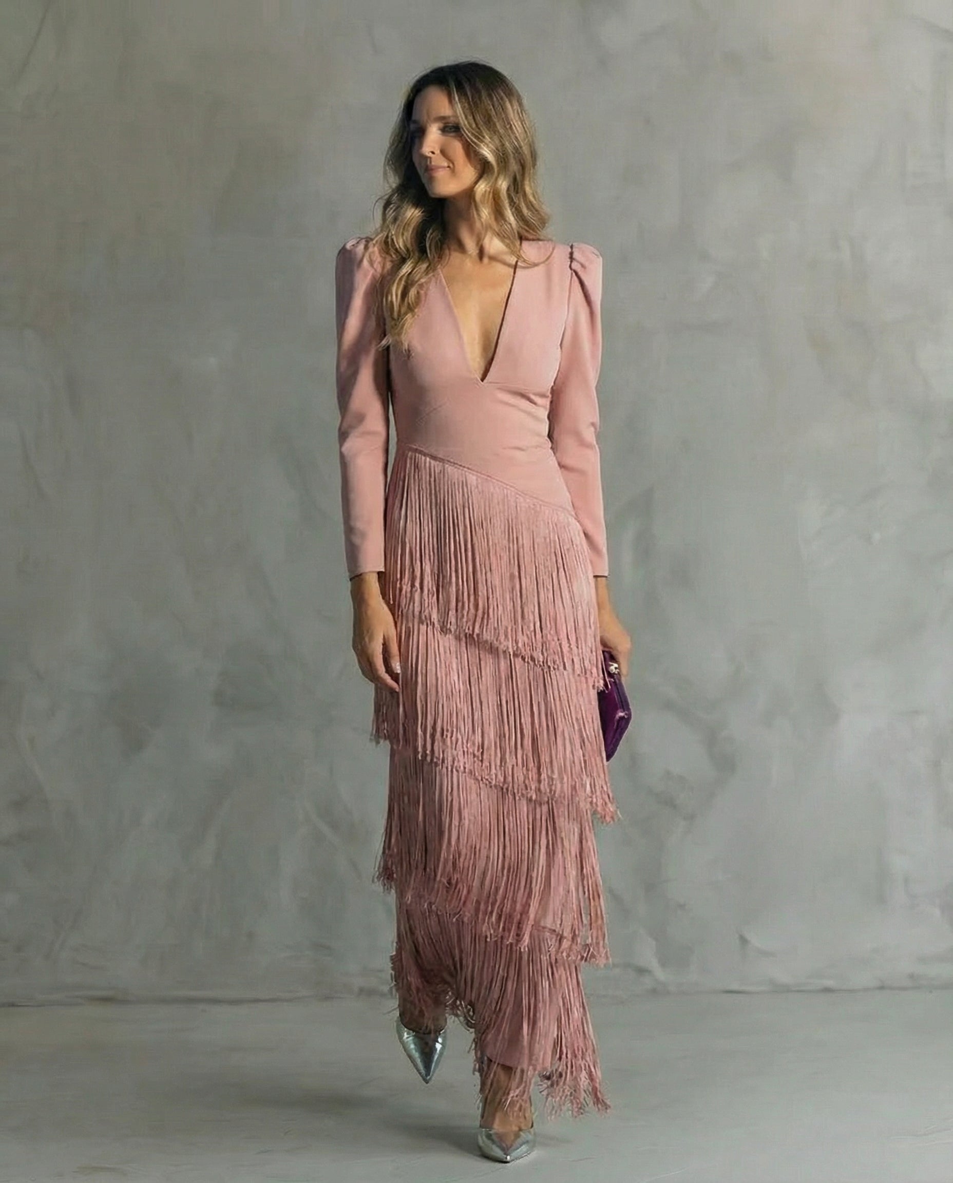 Woman wearing a pink dress with fringe details against a gray background