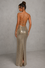 Woman wearing a sparkly gold evening gown with a backless design against a plain background