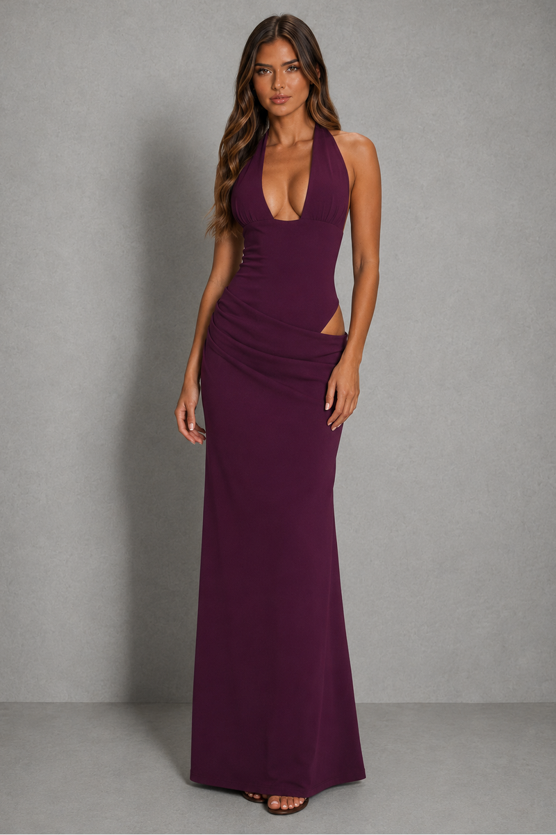 A woman modeling a sleeveless, deep V-neck, floor-length plum purple gown with side cutouts, standing against a neutral gray studio backdrop.