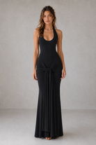 Woman wearing a black sleeveless gown with a knot detail on a plain background