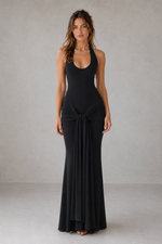 Woman wearing a black sleeveless gown with a knot detail on a plain background