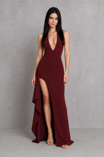 Woman wearing a burgundy evening gown with a high slit on a gray background