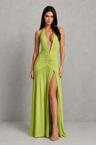 Woman wearing a green halter neck dress with a high slit on a gray background