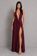 Woman wearing a burgundy evening gown with a high slit on a gray background