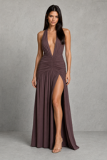 Woman wearing a deep-v, halter-neck dress with a high slit on a gray background
