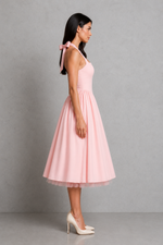 Woman wearing a pink dress with a bow detail on a gray background