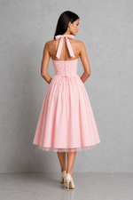 Woman wearing a pink dress with a bow detail on the back against a gray background