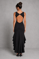 Woman wearing a black dress with an open back against a gray background