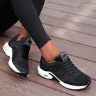 Black athletic shoes with white soles worn on a wooden floor