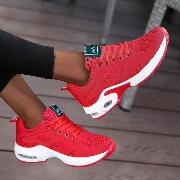 Red sneakers with white soles worn by a person on a wooden floor.