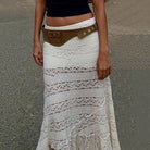 Person wearing a white lace skirt with a brown belt on a gray background