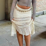 Person wearing a white lace skirt with a chain detail in an outdoor setting.