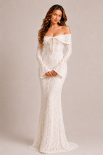 Woman wearing a white lace off-shoulder gown against a plain background