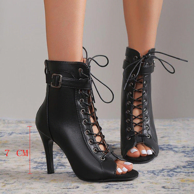 Black lace-up high-heeled shoes worn by a person on a neutral background