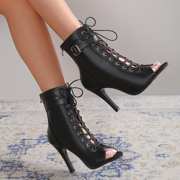 Black lace-up high-heeled boots worn by a person on a patterned rug.