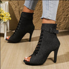 Black high-heeled peep-toe boots with lace-up design worn by a person.
