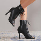 Black high-heeled lace-up boots worn by a person on a neutral background
